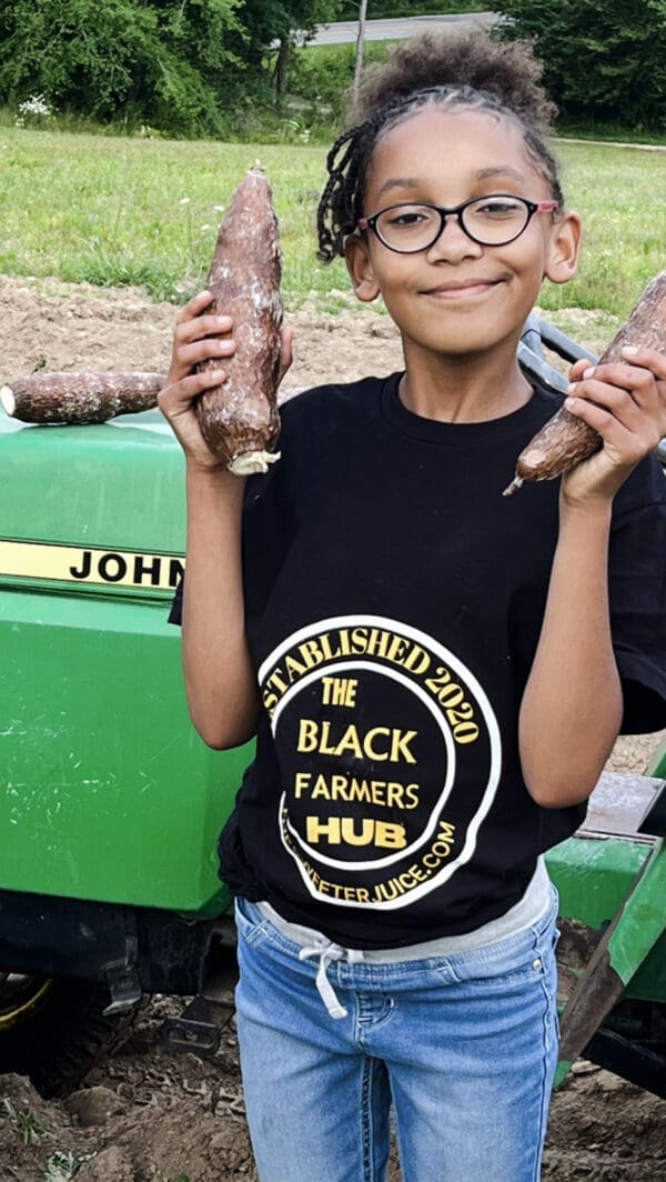 A young boy holding two turnips in front of a john deere tractor.